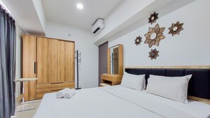 A hotel room with a large bed, wooden wardrobe, a vanity with a mirror, and decorative wall art.