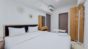 A modern hotel room with a large bed, a wooden wardrobe, a small table, and a mirror. - Nice And Homey 3Br Tamansari Bintaro Masion Apartment (South Tangerang)