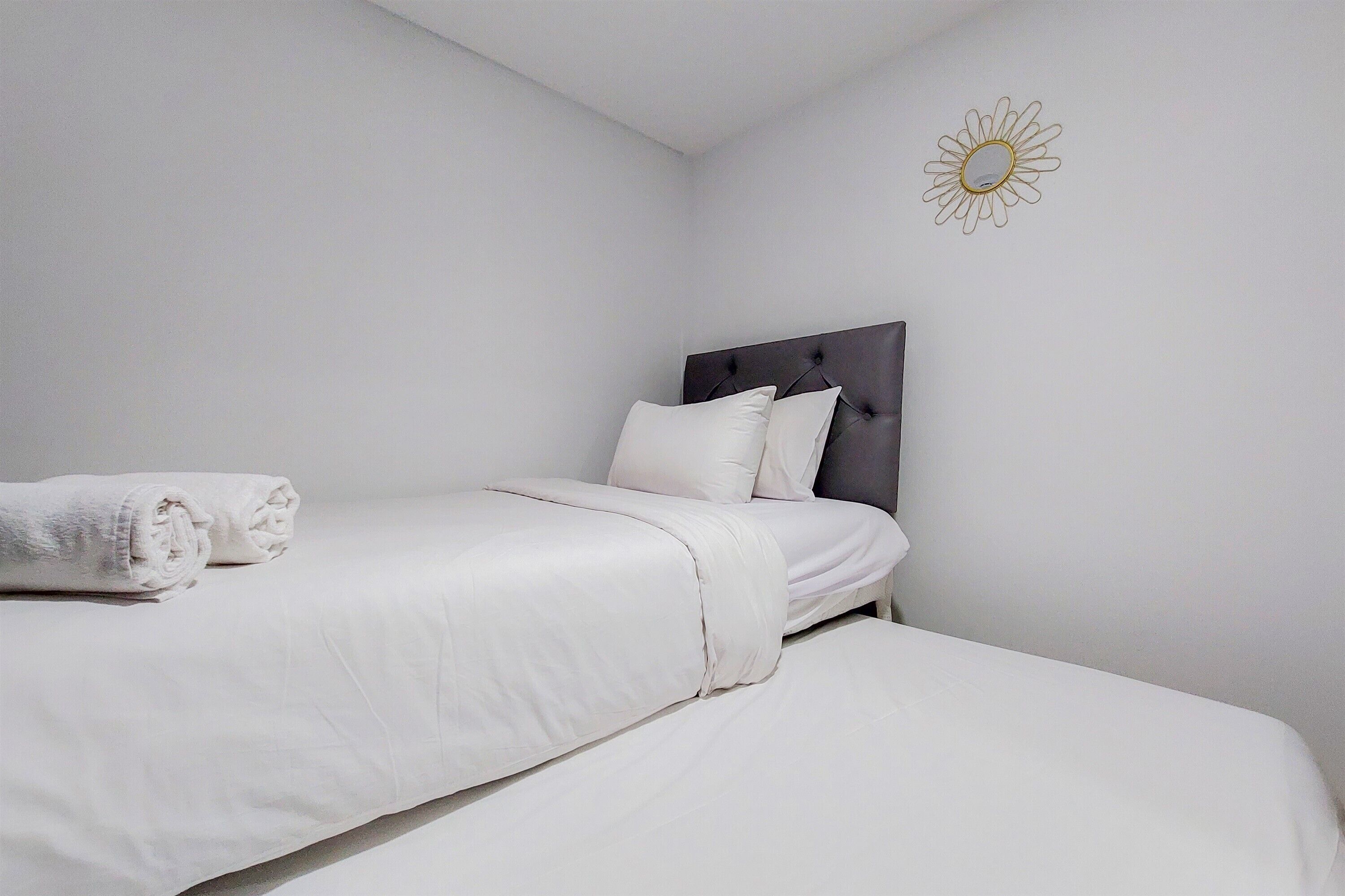 A neatly made bed with white linens and a rolled towel, a dark headboard, and a wall-mounted sun decoration.