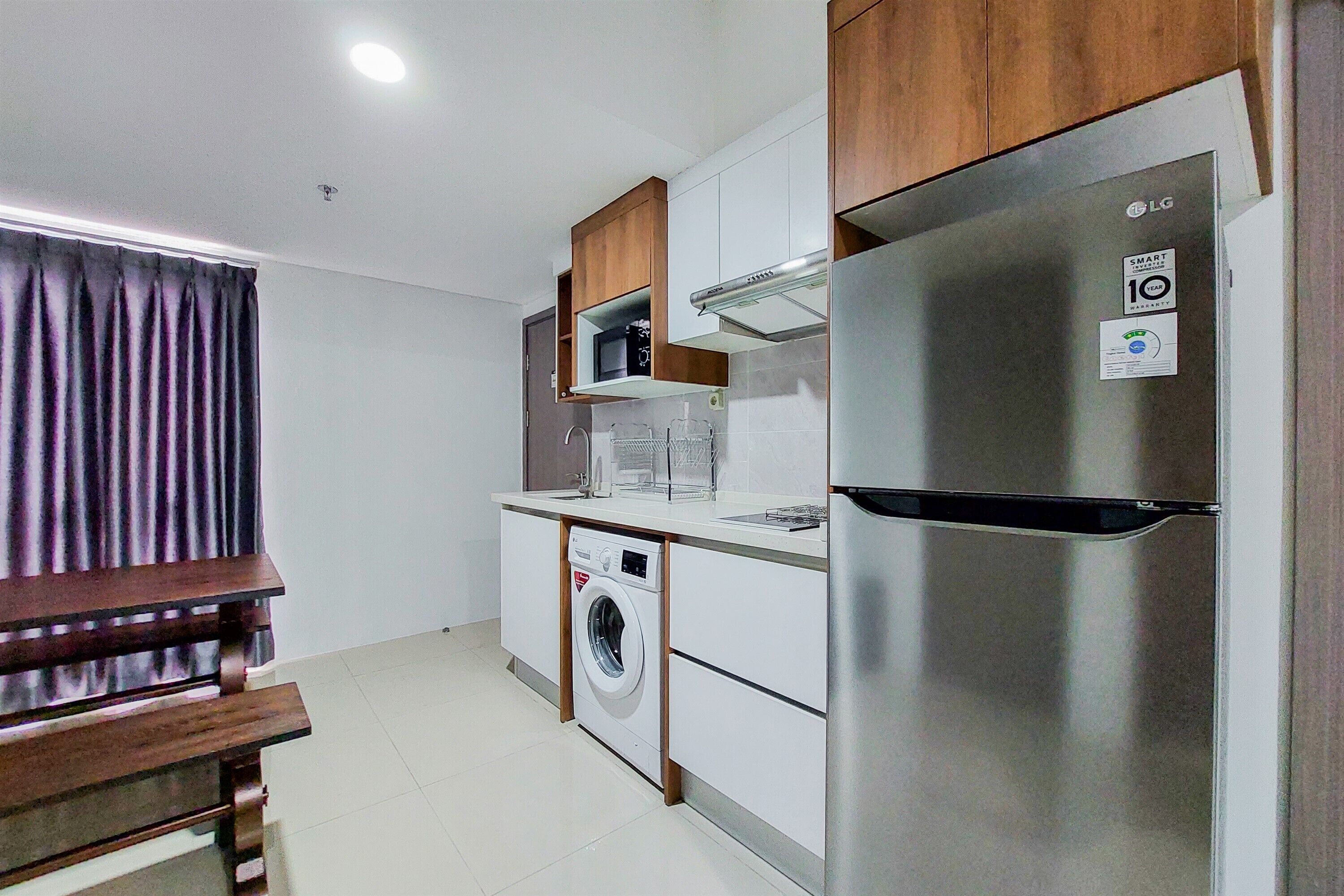 A compact kitchen with a stainless steel refrigerator, a built-in washing machine, and wooden cabinets.