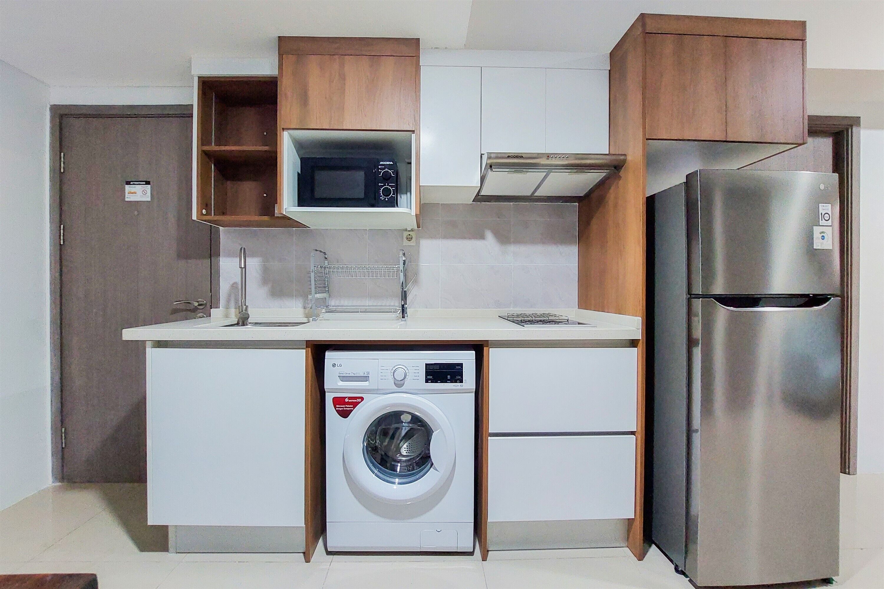 A compact kitchen with a built-in washing machine, a microwave, and a stainless steel refrigerator.
