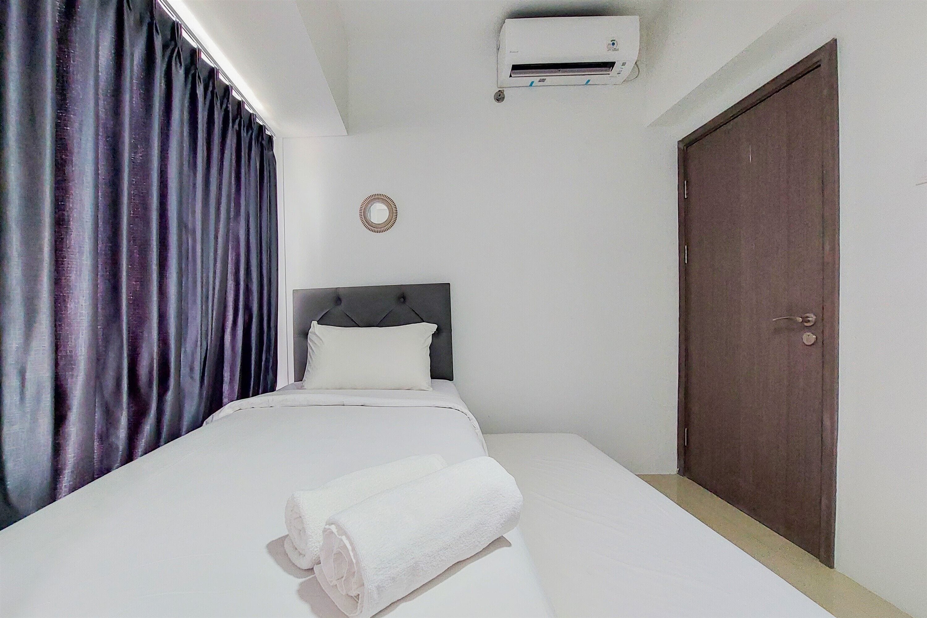 Una habitación de hotel con una cama, una puerta de madera oscura, un equipo de aire acondicionado blanco y cortinas moradas.