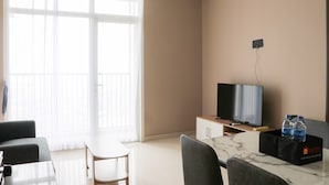 A hotel room with a large window, a flat-screen TV, a dining table, and a seating area. - Modern And Compact Designed 1Br At Ciputra International Apartment (Jakarta)