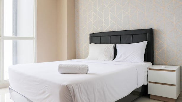 A neatly made bed with white linens and a folded towel, a bedside table with a drawer, and a geometric patterned wall. - Modern And Compact Designed 1Br At Ciputra International Apartment (Jakarta)