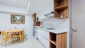 A compact kitchen with a dining table and chairs, a washing machine, and wooden shelves.
