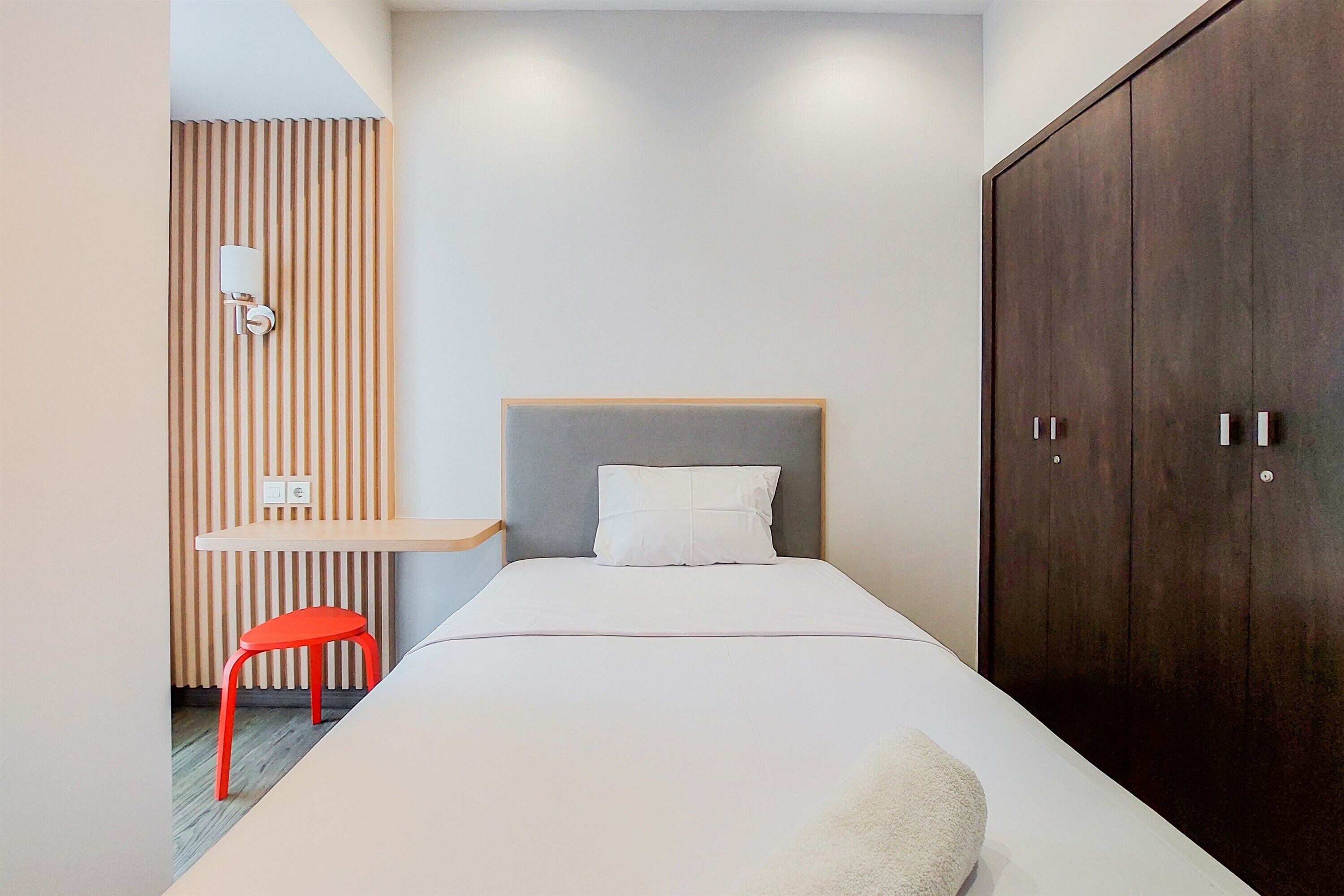 A bedroom with a bed, a wardrobe, a desk, and a red chair.