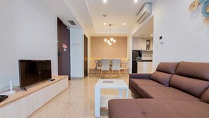 Una sala moderna con televisor de pantalla plana, un sofá, una mesita de centro y una zona de comedor con sillas y un fondo de madera.