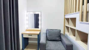 A compact room with a desk, a chair, a mirror with lights, and built-in shelving. - Cozy Stay Studio At Mataram City Apartment (Ngaglik)