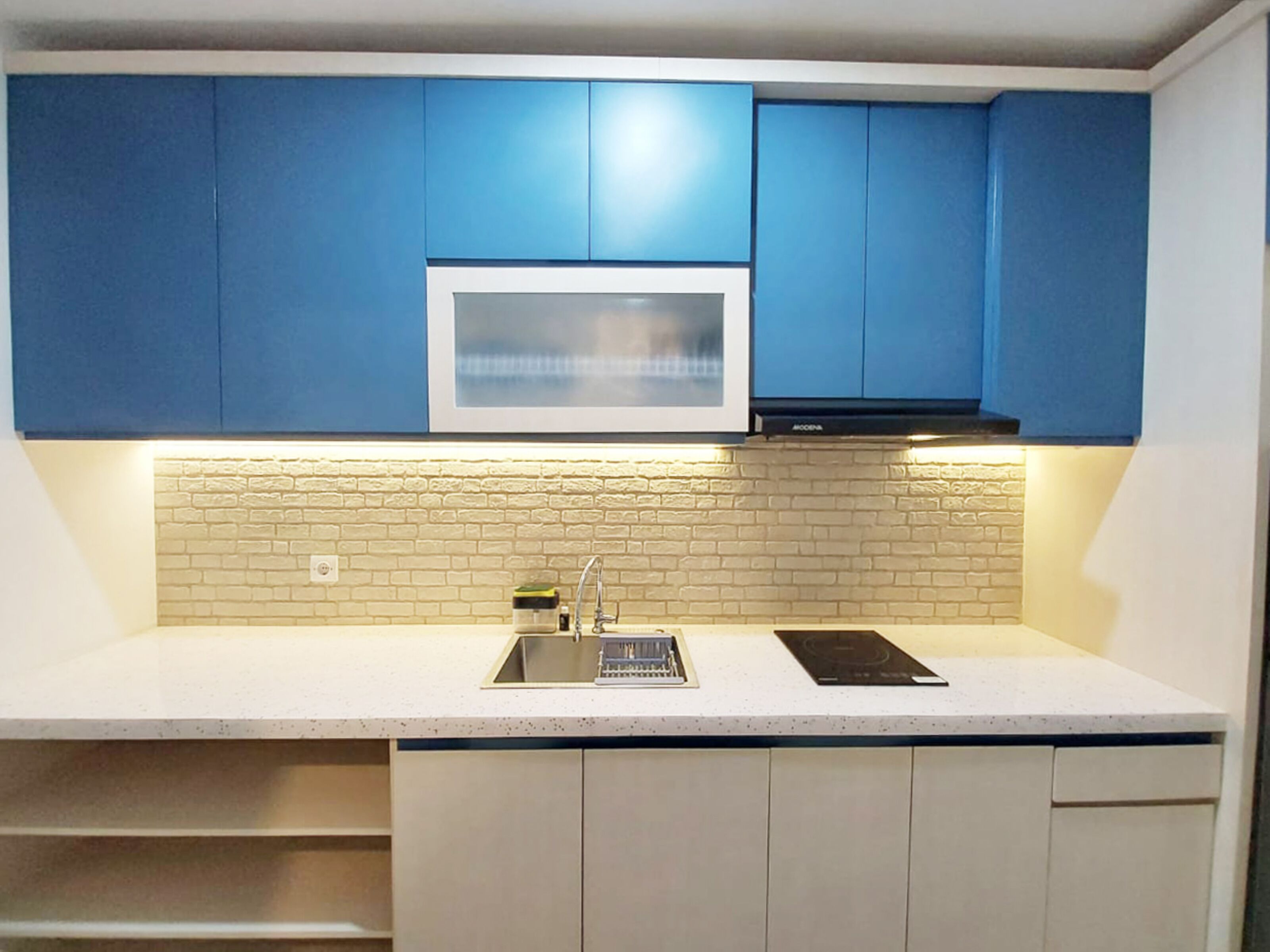 Una cocina con armarios azules, microondas, pileta y lavavajillas.