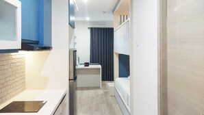 A narrow hotel corridor with a kitchenette on the left, a small bathroom with a shower and toilet, and a bedroom with a bed and curtains on the right. - Cozy Stay Studio At Mataram City Apartment (Ngaglik)