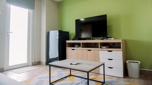A room with a TV on a wooden cabinet, a small table, and a trash bin. - Well Furnished And Cozy Studio Baileys Apartment (South Tangerang)