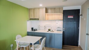 A compact kitchen with a white table and chairs, wooden cabinets, and a dark door. - Well Furnished And Cozy Studio Baileys Apartment (South Tangerang)