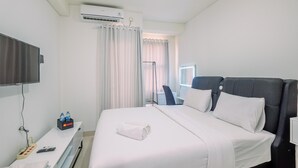 A hotel room with a bed, a desk with a remote control, a water bottle, and a TV. - Simply Look Studio At Transpark Cibubur Apartment (Bekasi)