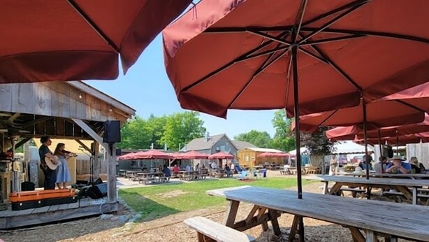 An outdoor market with wooden tables and red umbrellas. - Between Crystal Mountain & TC - Barn - Guest house on 10acres. Pet-friendly! (Interlochen)