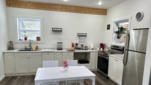 A modern kitchen with white cabinetry, a stainless steel refrigerator, and a dining area with a white table and bench. - Between Crystal Mountain & TC - Barn - Guest house on 10acres. Pet-friendly! (Interlochen)