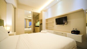A hotel room with a large bed, a TV mounted on the wall, a mirror, and a small shelf with toiletries. - Warm Designed Studio At Orchard Supermall Mansion Apartment (Surabaya)