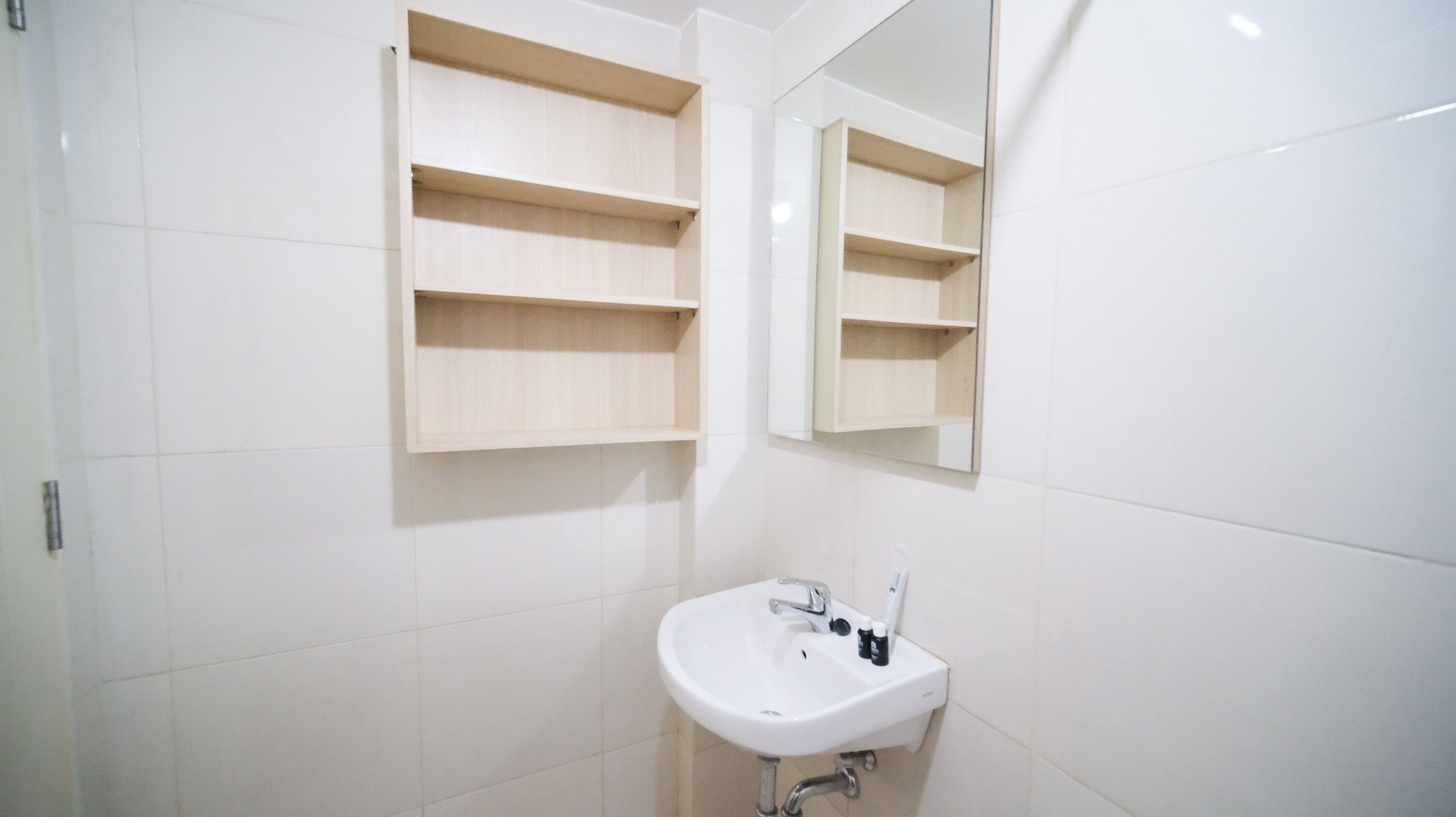 Een badkamer met witte tegels, een wit wastafelmeubel en houten planken boven de spiegel.