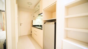 A narrow kitchen with white cabinets, a refrigerator, and a sink. - Warm Designed Studio At Orchard Supermall Mansion Apartment (Surabaya)