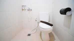 Un baño pequeño y blanco con inodoro, ducha y dispensador de papel higiénico.