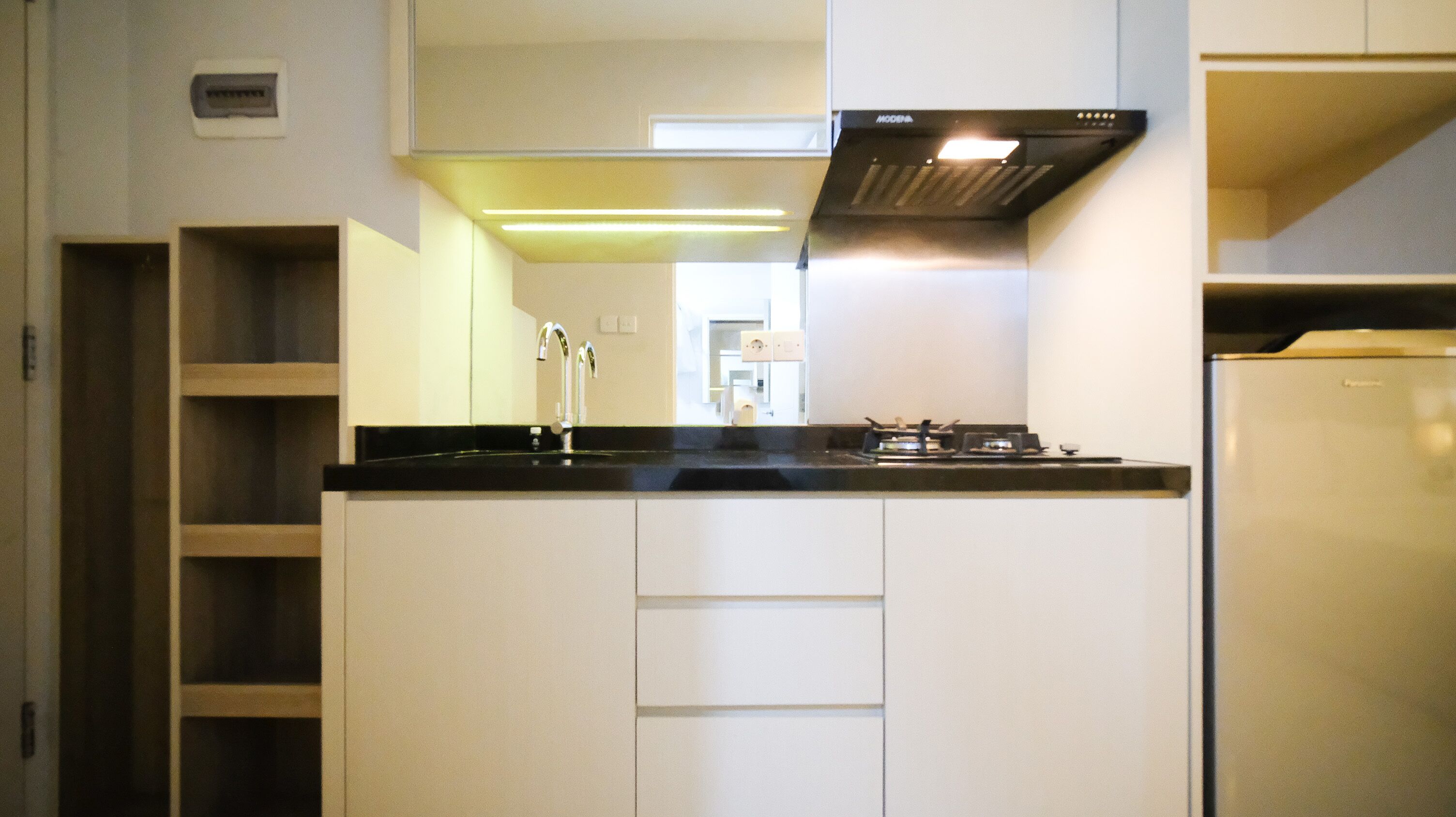 A modern kitchen with white cabinetry, a black countertop, a stainless steel range hood, and a built-in refrigerator.