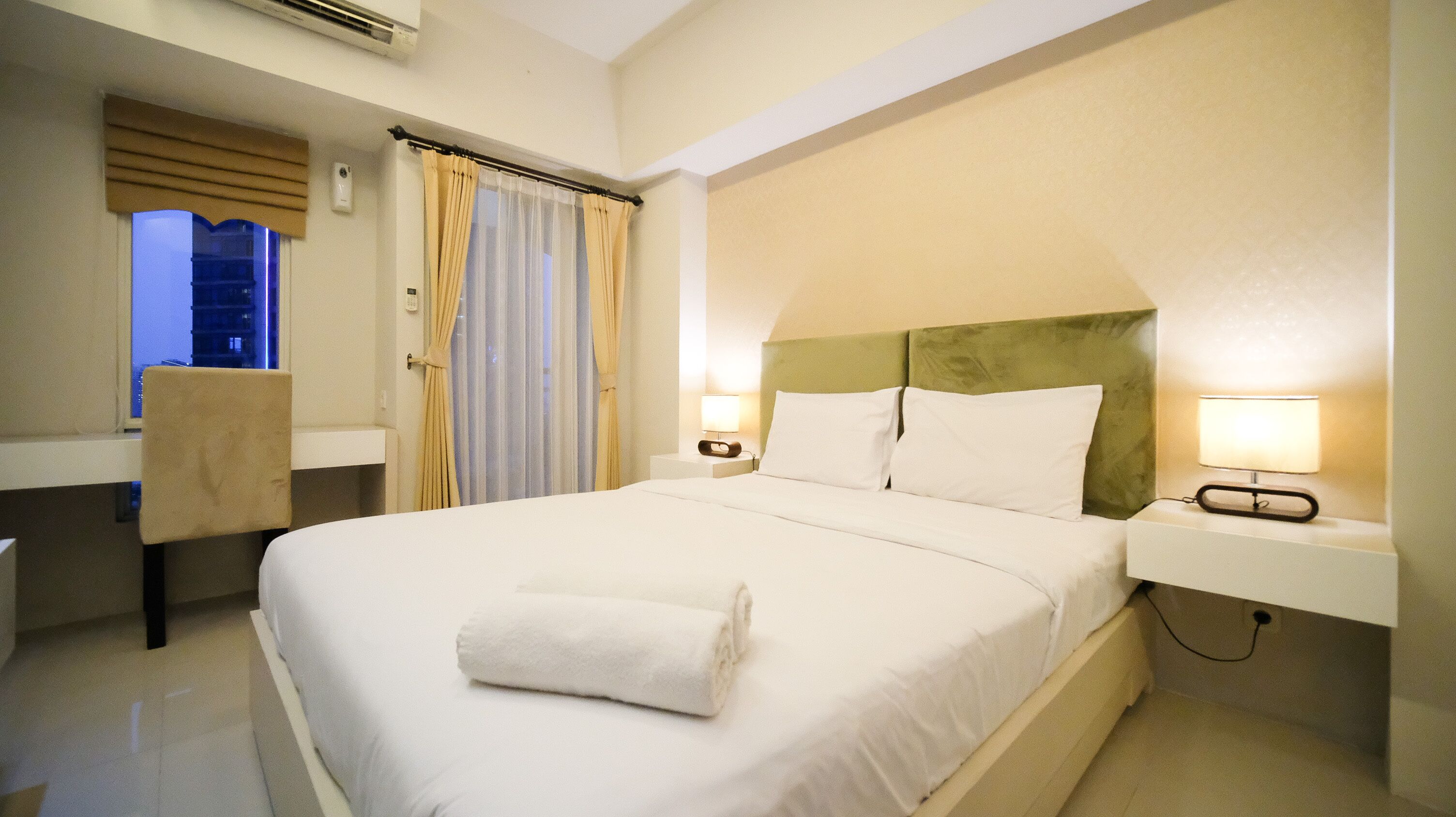 A hotel room with a large bed, a chair, a nightstand with a lamp, and a window with curtains.