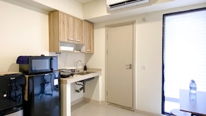 A compact kitchen with a refrigerator, microwave, and sink. There is a sliding door leading to a balcony with a table and chairs. - Best Choice And Tidy Studio Meikarta Apartment (Cikarang)