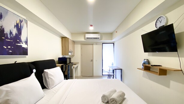A hotel room with a bed, a desk, a chair, a TV, and a door leading to a balcony. - Best Choice And Tidy Studio Meikarta Apartment (Cikarang)