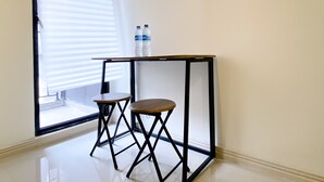 A corner room with a small table and two stools, a window with blinds, and two water bottles on the table. - Best Choice And Tidy Studio Meikarta Apartment (Cikarang)