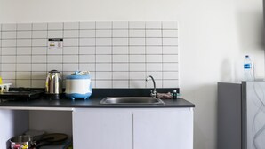 A kitchen with a sink, a kettle, a toaster, and a water bottle on the counter. - Cozy And Comfort Stay Studio Sayana Bekasi Apartment (Tarumajaya)