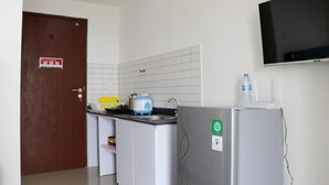A kitchen with a wooden door, a white tiled backsplash, a grey refrigerator, a blue toaster, and a water dispenser. - Cozy And Comfort Stay Studio Sayana Bekasi Apartment (Tarumajaya)