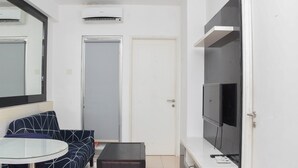 Un salon moderne comprenant un canapé, une table en verre, un pouf foncé, un téléviseur à écran plat et une porte avec un cadre blanc.