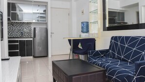 Un salon moderne avec un canapé bleu, une table basse et un coin cuisine équipé d’un réfrigérateur et doté d’un plan de travail recouvert de carreaux.