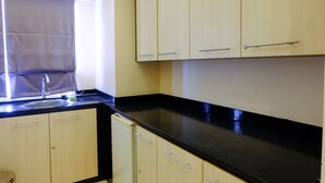 Una cocina con armarios de madera clara, encimera negra y ventana con persiana.