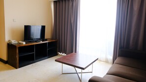 Una sala de estar con una televisión de pantalla plana sobre un mueble de madera, una mesita pequeña y un sofá marrón.