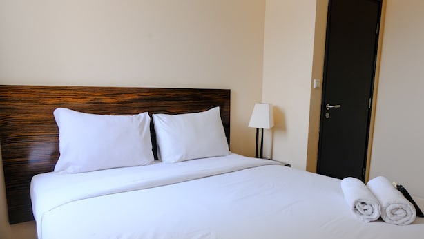 Una cama bien hecha con sábanas blancas y dos almohadas, una lámpara en una mesita de noche y dos toallas enrolladas sobre la cama.