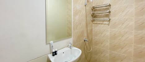 A bathroom with a white sink, a mirror, a shower, and a towel rack.