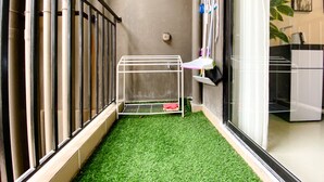 A small room with artificial green carpet, a metal rack, and a window with blinds. - Spacious And Homey 2Br At Meikarta Apartment (Cikarang)