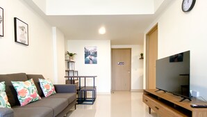 A modern living room with a grey sofa, colorful pillows, a wooden TV stand, and a flat-screen TV. - Spacious And Homey 2Br At Meikarta Apartment (Cikarang)