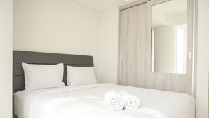 A neatly made bed with white linens and two rolled towels, a dark headboard, and a large mirror on the wall. - Wonderful And Homey 2Br At Gold Coast Apartment (Jakarta)
