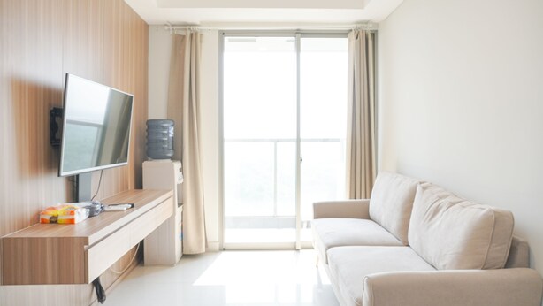 A modern living room with a flat-screen TV, a wooden cabinet, a water dispenser, and a beige sofa. - Wonderful And Homey 2Br At Gold Coast Apartment (Jakarta)