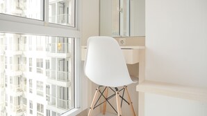 A modern room with a large window, a white chair, and a wooden floor. - Simply Studio At 18Th Floor Tokyo Riverside Pik 2 Apartment (Teluknaga)