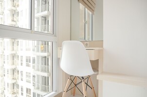 Quarto moderno com uma janela grande, uma cadeira branca e piso de madeira.