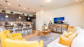A modern living room with a sofa, yellow chairs, a coffee table, and a TV. - Lakeview Resort Home, Private Pool, Gym, Game Room (Kissimmee)