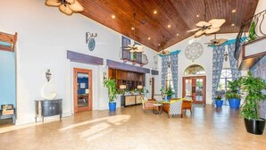 A spacious lobby with a high ceiling, wooden beams, and multiple ceiling fans. There are several potted plants and a reception desk with a counter. - Lakeview Resort Home, Private Pool, Gym, Game Room (Kissimmee)