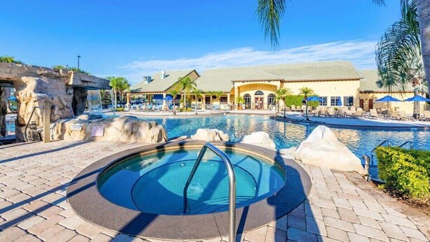 A pool area with a hot tub, lounge chairs, and a building with a tiled roof. - Lakeview Resort Home, Private Pool, Gym, Game Room (Kissimmee)