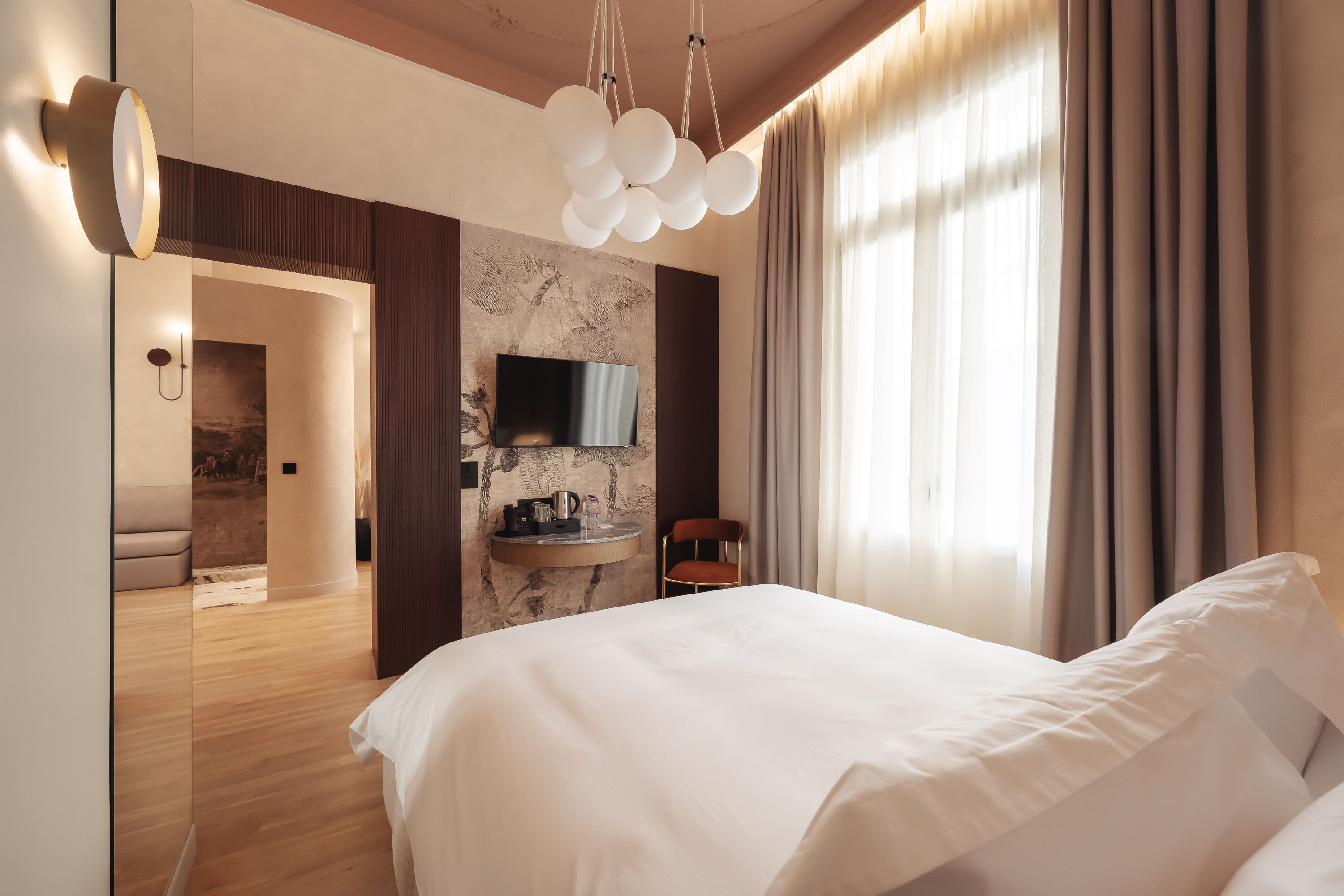 Una habitación de hotel moderna con una cama grande, un televisor de pantalla plana en una pared de mármol, un espejo redondo y suelo de madera.