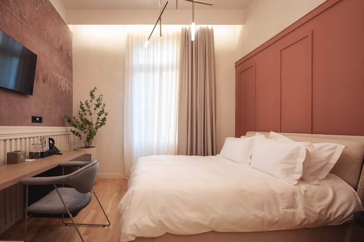 Habitación de hotel moderna con una cama, un escritorio con silla, una planta en maceta y un televisor montado en la pared.