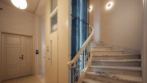 A staircase with marble steps and a metal railing, leading to a landing with a door and a light fixture.