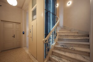 A staircase with marble steps and a metal railing, leading to a landing with a door and a light fixture.