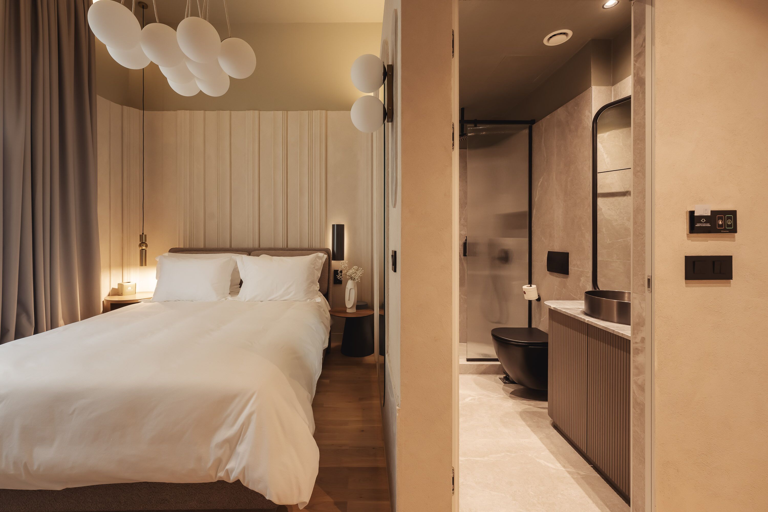Une chambre d’hôtel moderne avec un grand lit, une table de chevet et une salle de bain équipée d’un miroir et d’un lavabo.